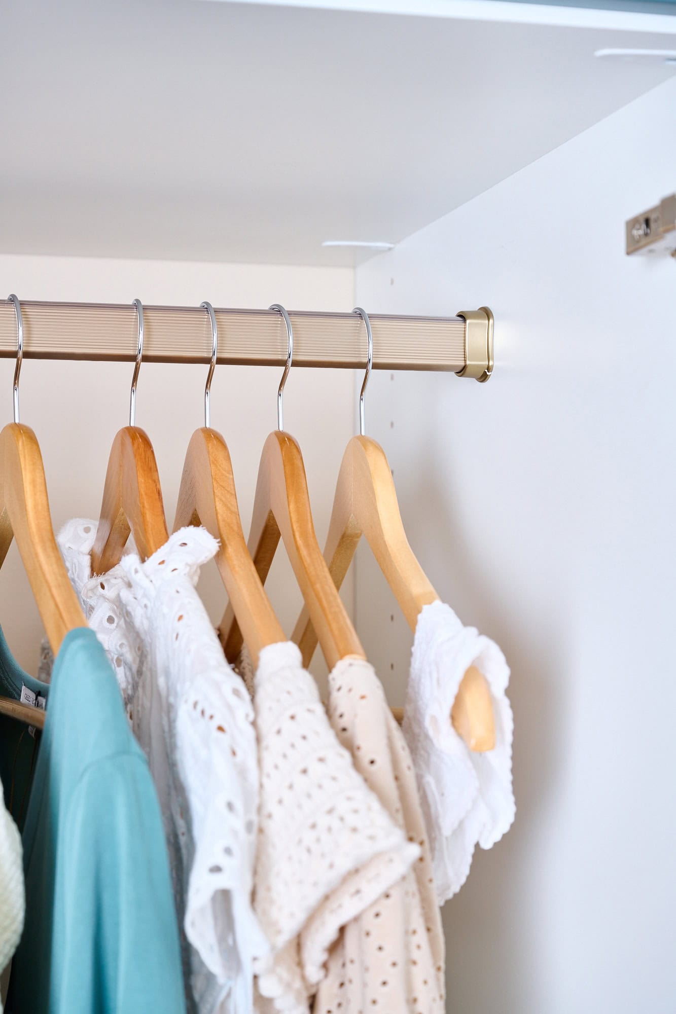 Clothes hanging in a closet with wooden hangers and a metal clothing rod, showcasing organized interior storage.